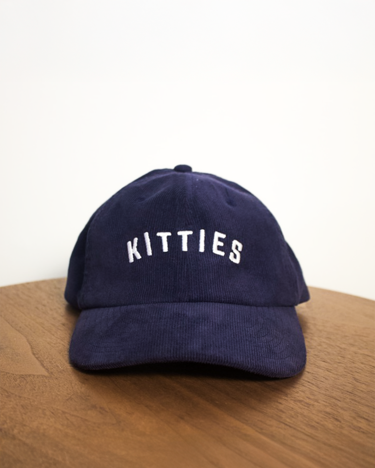 Navy blue cap with 'Kitties' text on a wooden surface