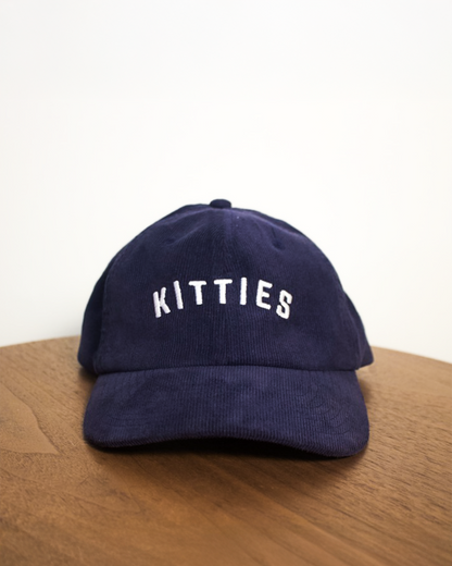 Navy blue cap with 'Kitties' text on a wooden surface